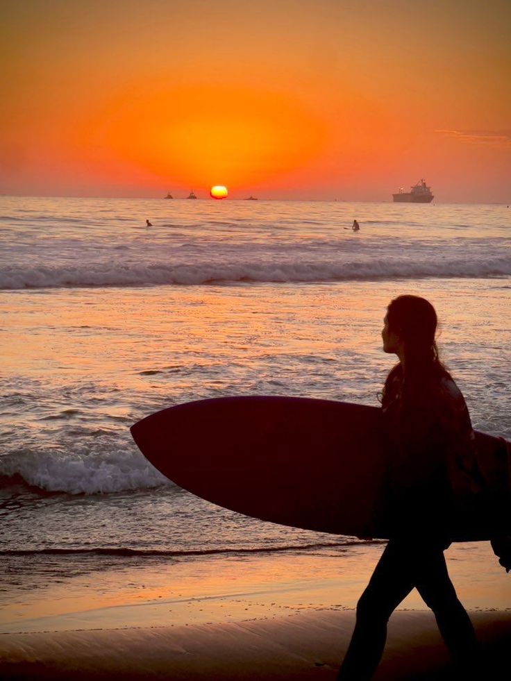 Surfer walking on the beach at sunset with a surfboard
