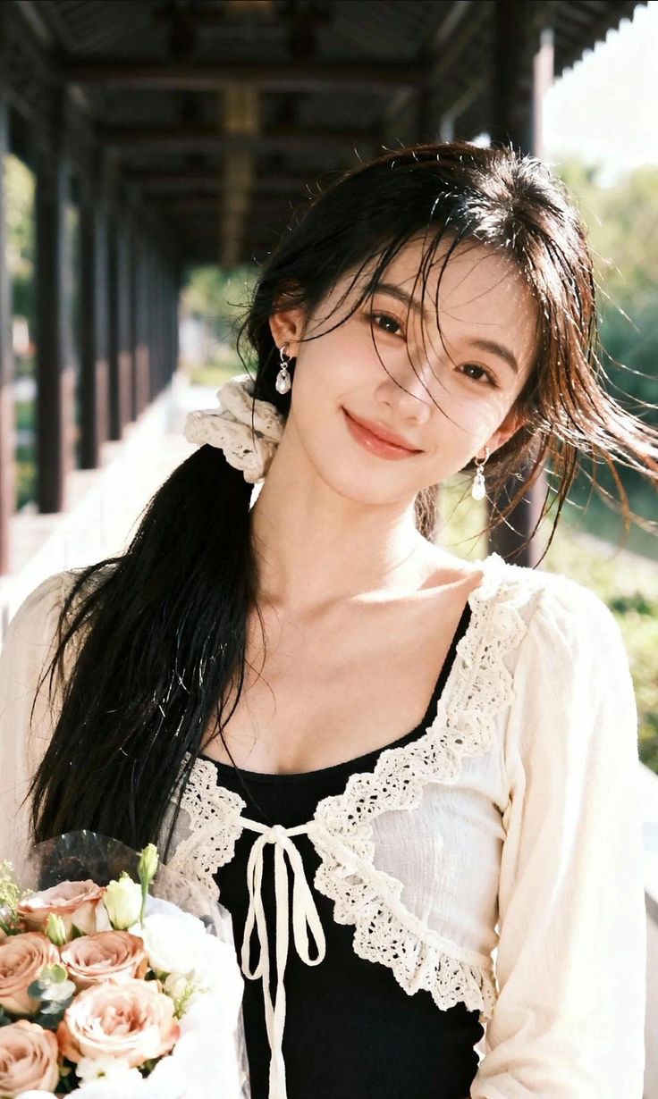 Woman with long hair in a lace top holding a bouquet outdoors