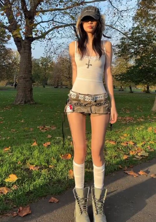 Woman in a mini skirt, tank top, and boots standing in a park