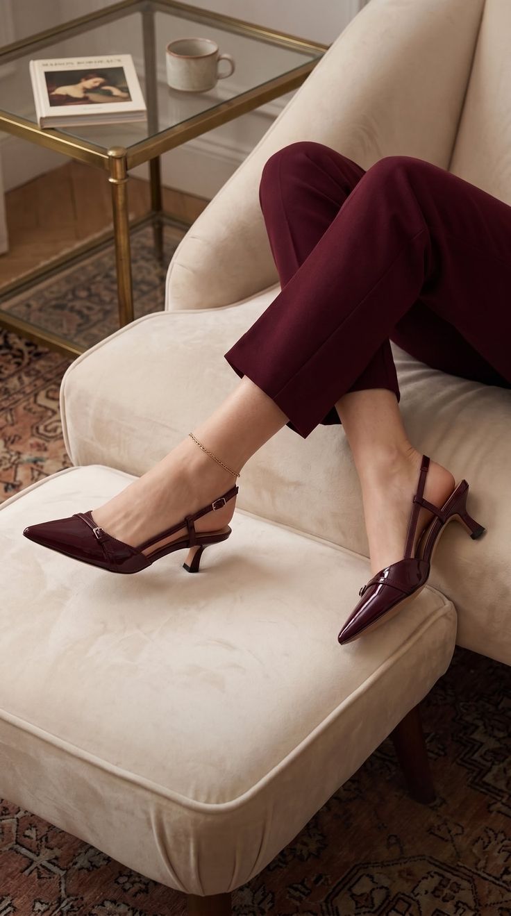 Person wearing burgundy pants and high heels, sitting on a cream-colored chair