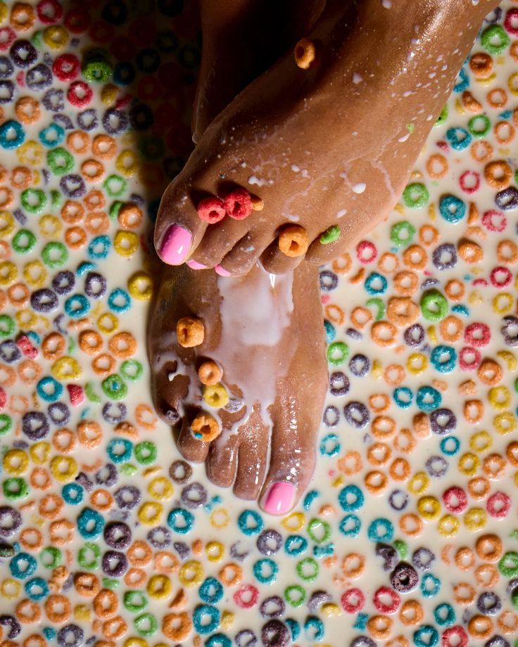 Feet with pink nail polish in a bowl of colorful cereal and milk