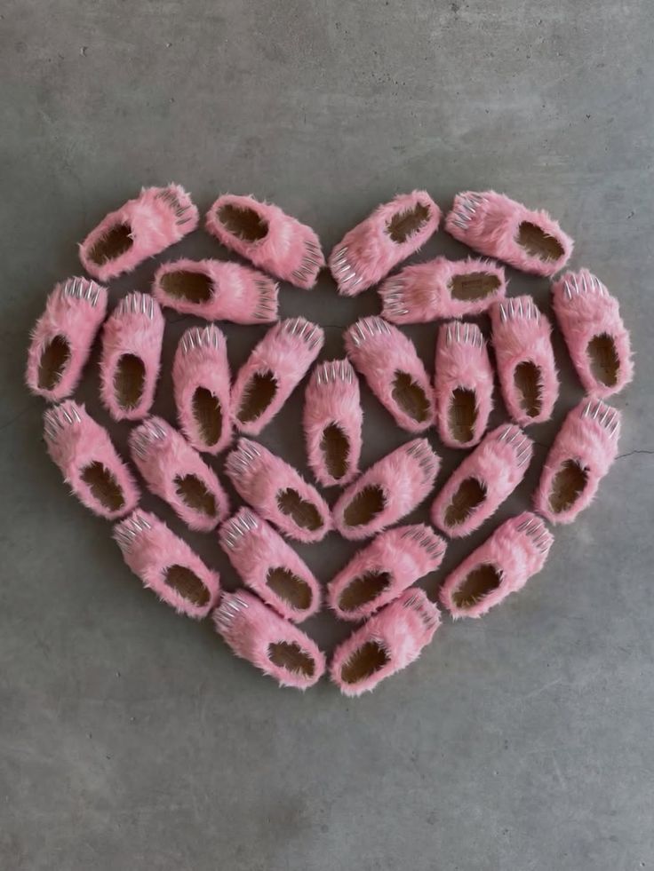 Pink fur slippers with silver claws arranged in a heart shape on a concrete floor