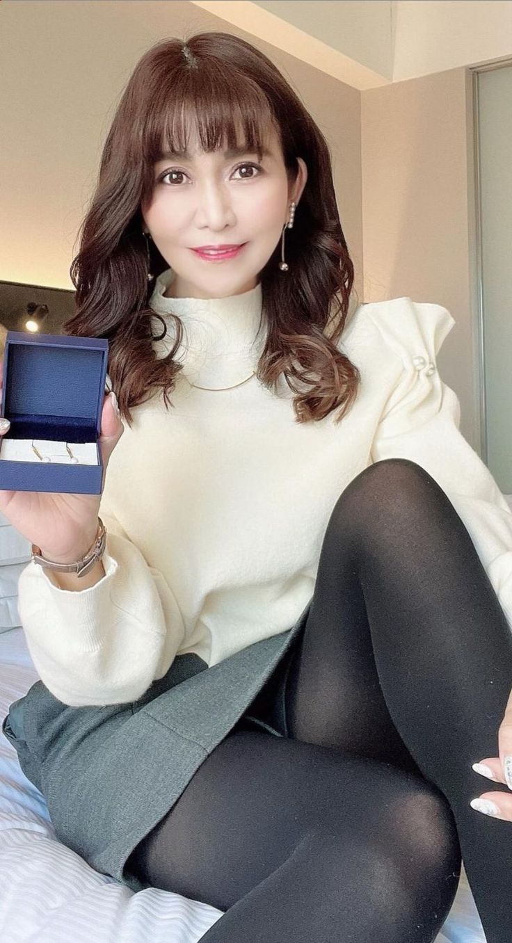 Woman in a white sweater and black tights holding a small blue box