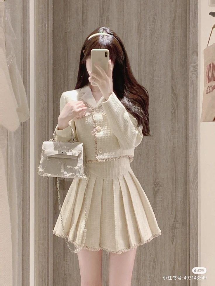 Person in a tweed jacket and pleated skirt taking a mirror selfie