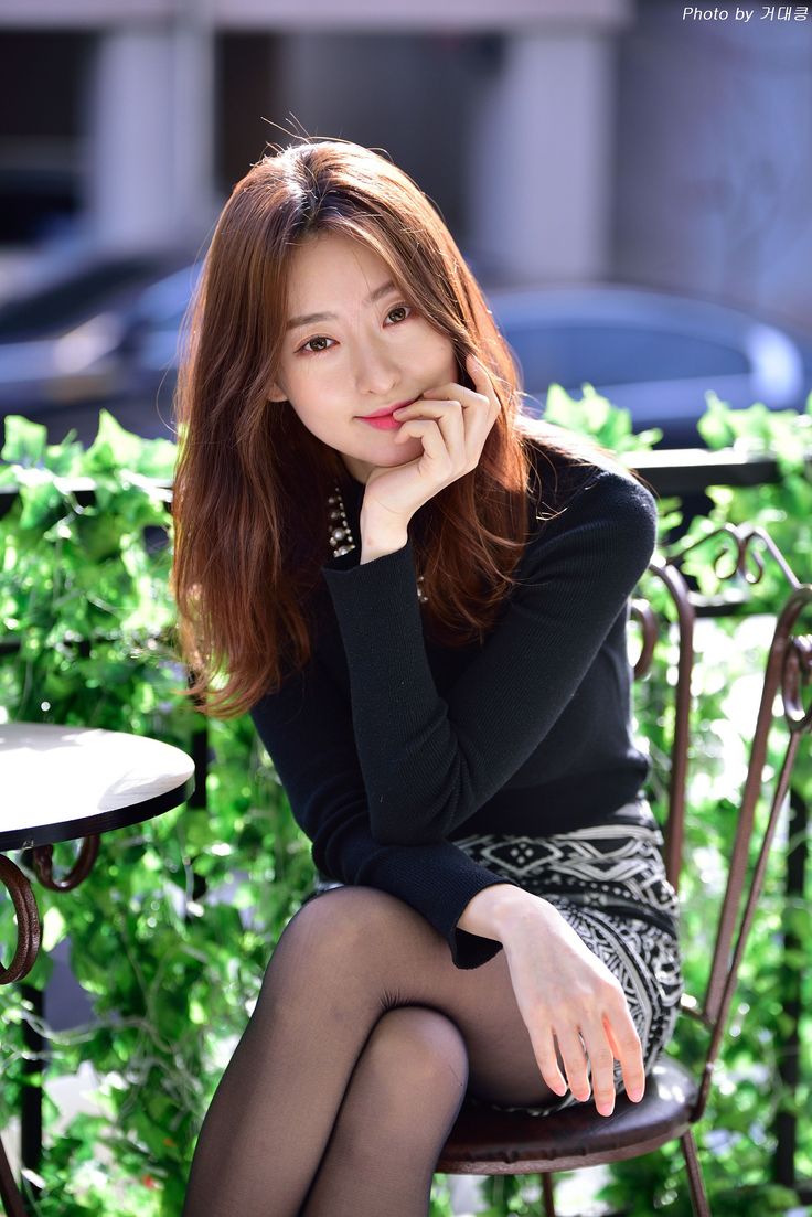 Woman with long hair in a black sweater and patterned skirt sitting outdoors