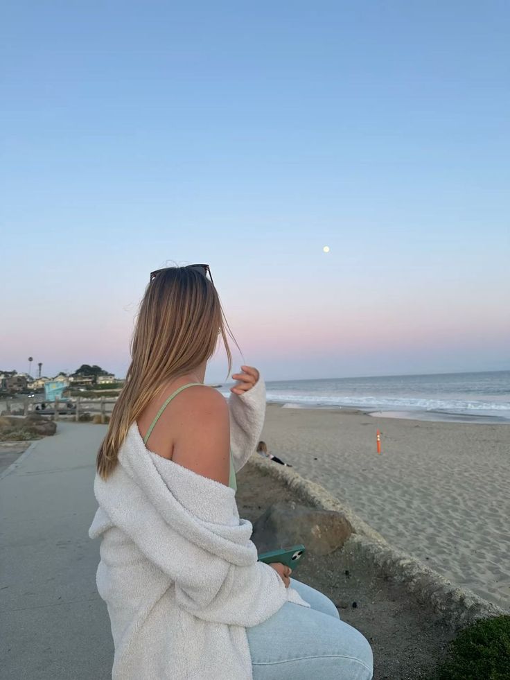 Woman with long hair looking at the moon over a beach at sunset