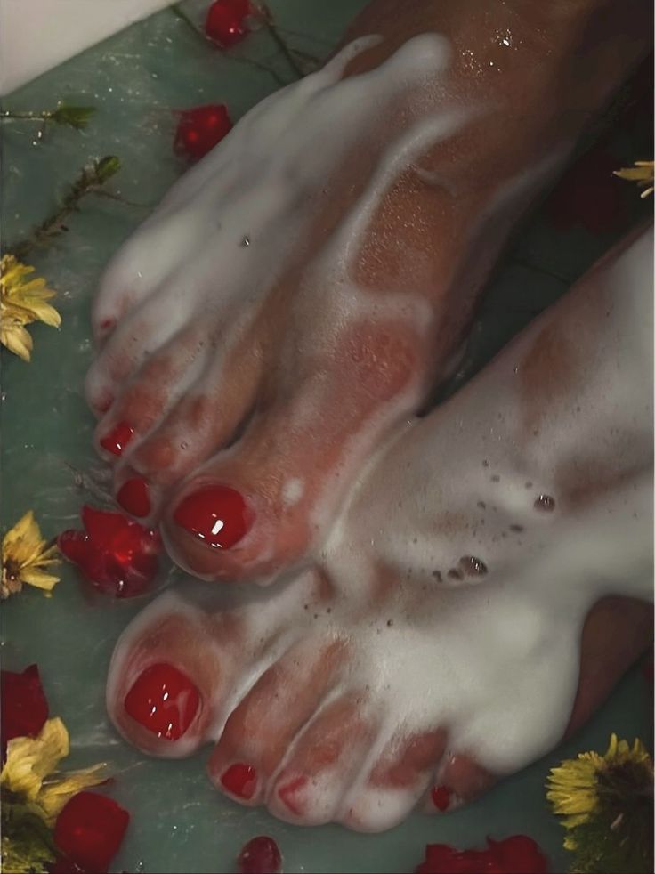 Feet with red nail polish in a bubble bath with flowers and petals