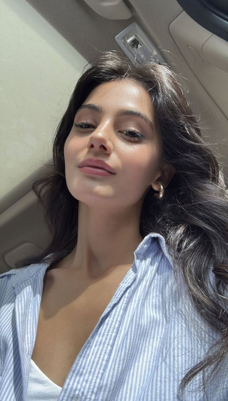 Woman with long dark hair wearing a striped shirt and gold hoop earrings indoors