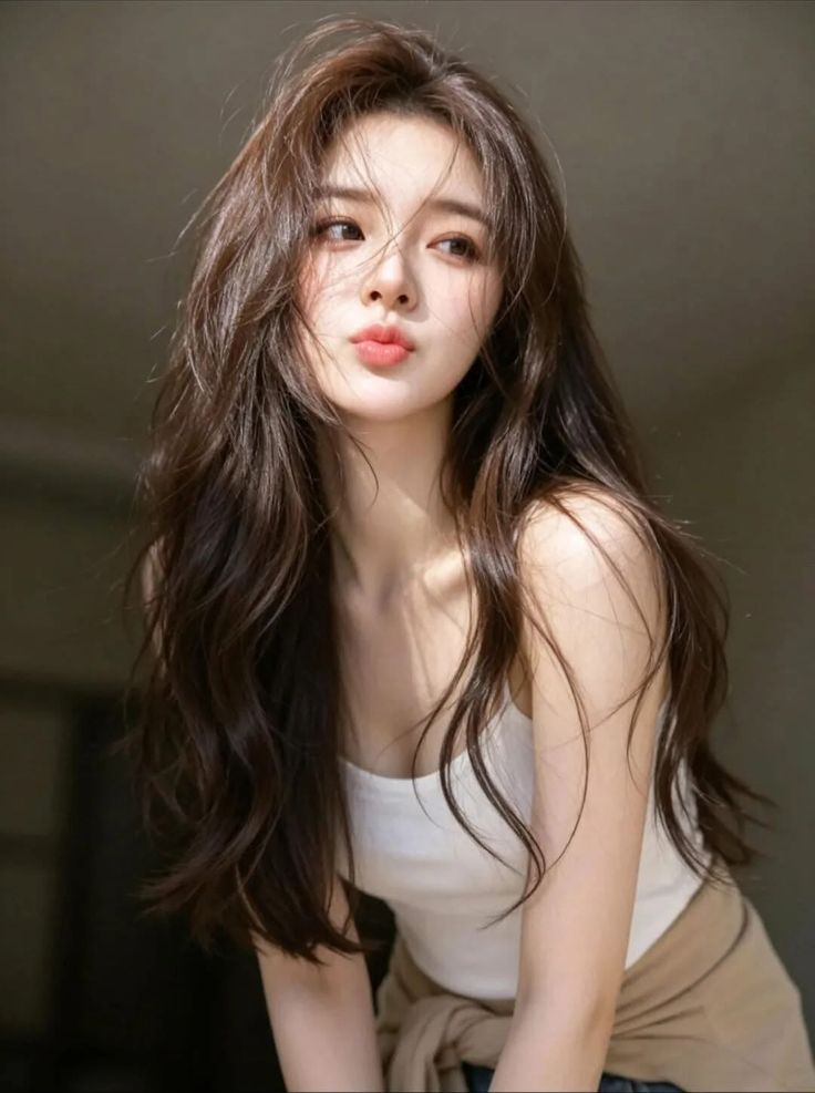 Woman with long brown hair and a white tank top making a pouty face