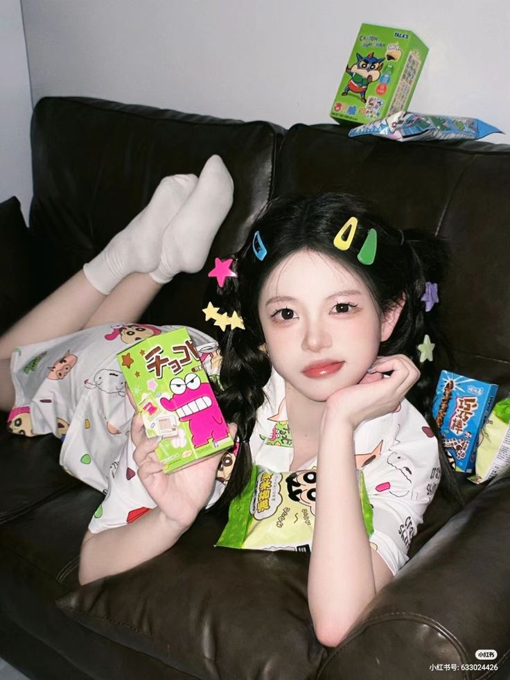Woman in pajamas with pigtails and colorful hair clips lying on a couch with snacks