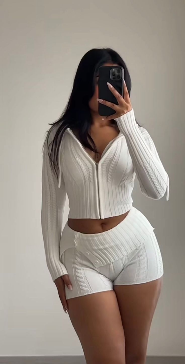 Woman in a white knitted cropped hoodie and shorts taking a mirror selfie