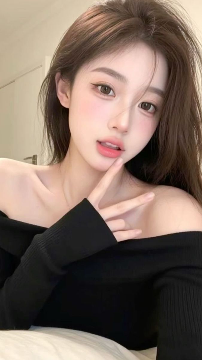 Woman with long brown hair wearing an off-shoulder top, making a peace sign