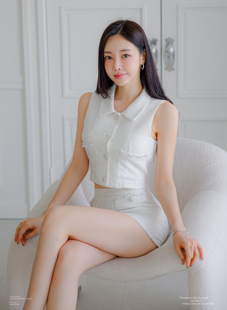 Woman in a white two-piece outfit sitting on a chair indoors