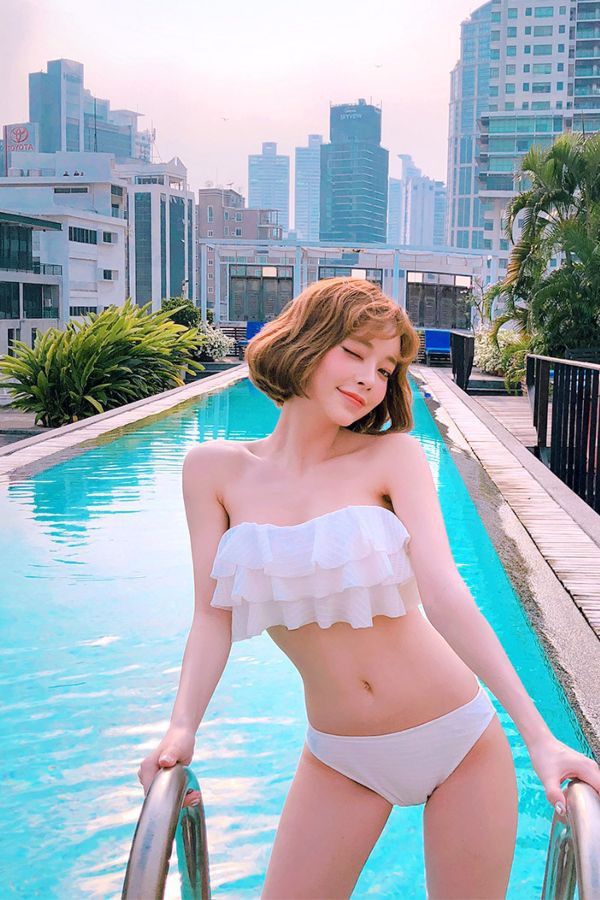 Woman in a white bikini posing by a rooftop pool with a cityscape background