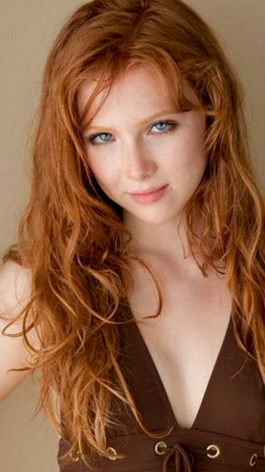 Woman with long red wavy hair and blue eyes wearing a brown top