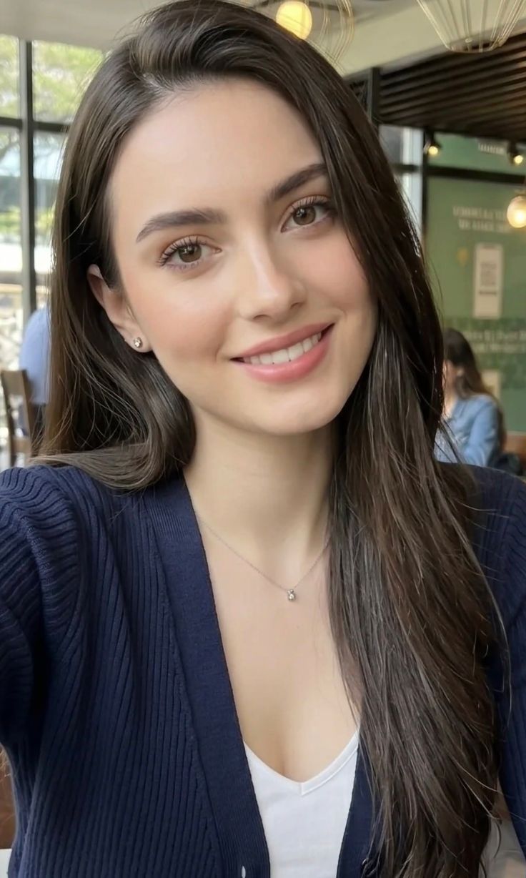 Smiling woman with long dark hair wearing a navy cardigan and white top indoors