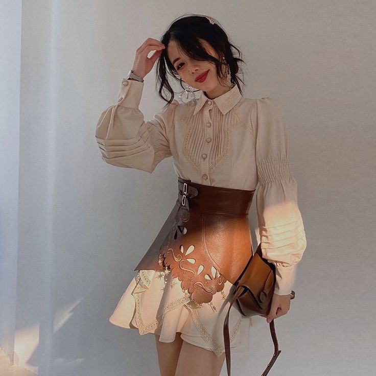 Woman in a long sleeve shirt and leather skirt holding a brown bag