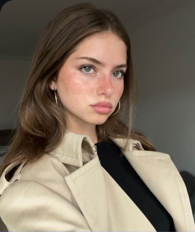 Woman with long hair and freckles wearing a trench coat and hoop earrings