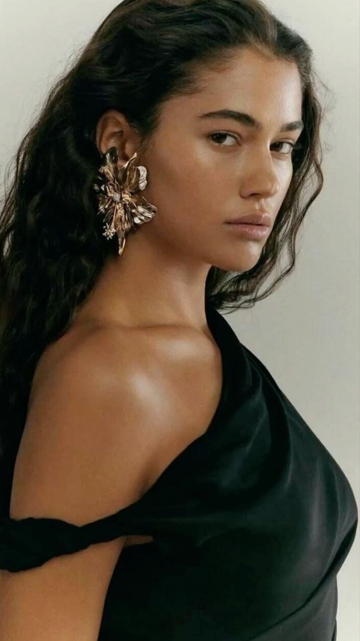Woman with long dark hair wearing a black dress and a large earring