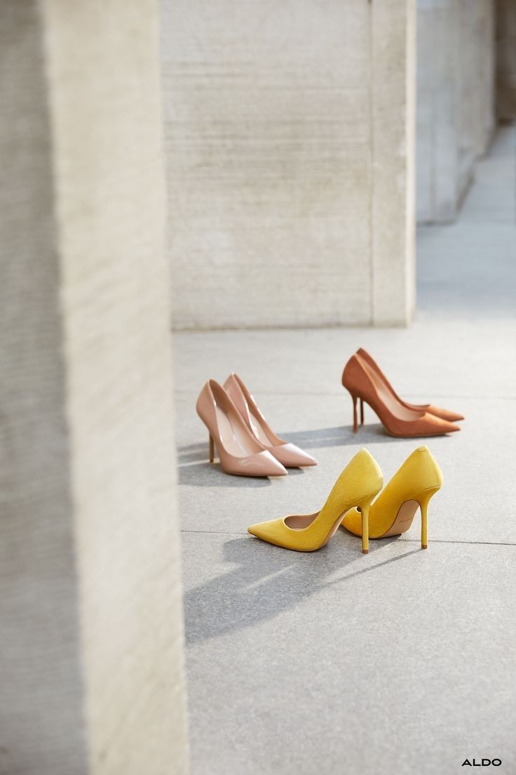 Three pairs of high heels in yellow, nude, and brown on a concrete surface