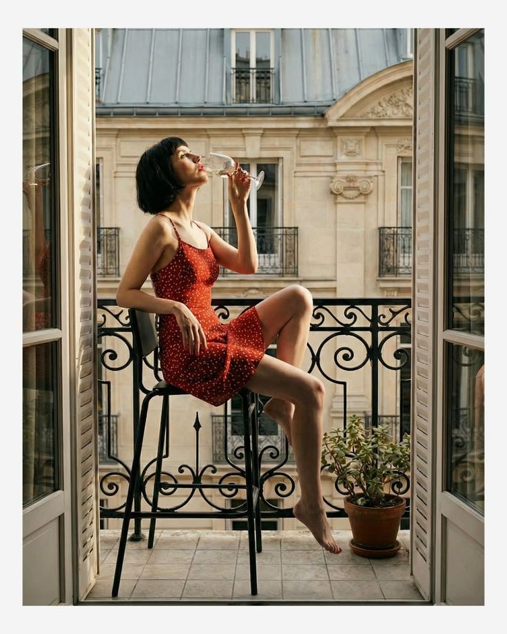 Woman in a red dress drinking wine on a balcony overlooking a cityscape