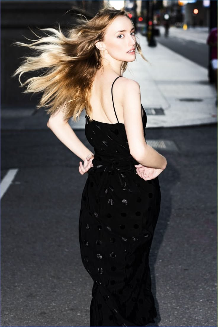 Woman in a black dress with long blonde hair blowing in the wind on a street