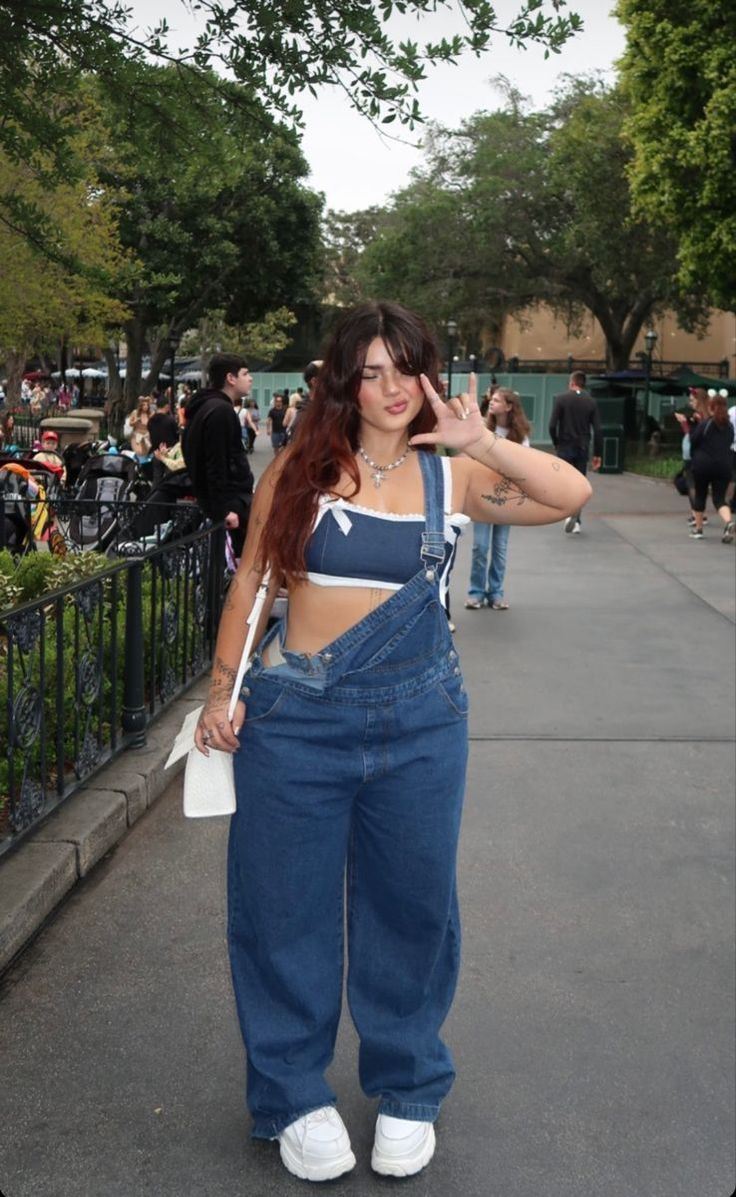 Woman in denim overalls and a crop top posing outdoors