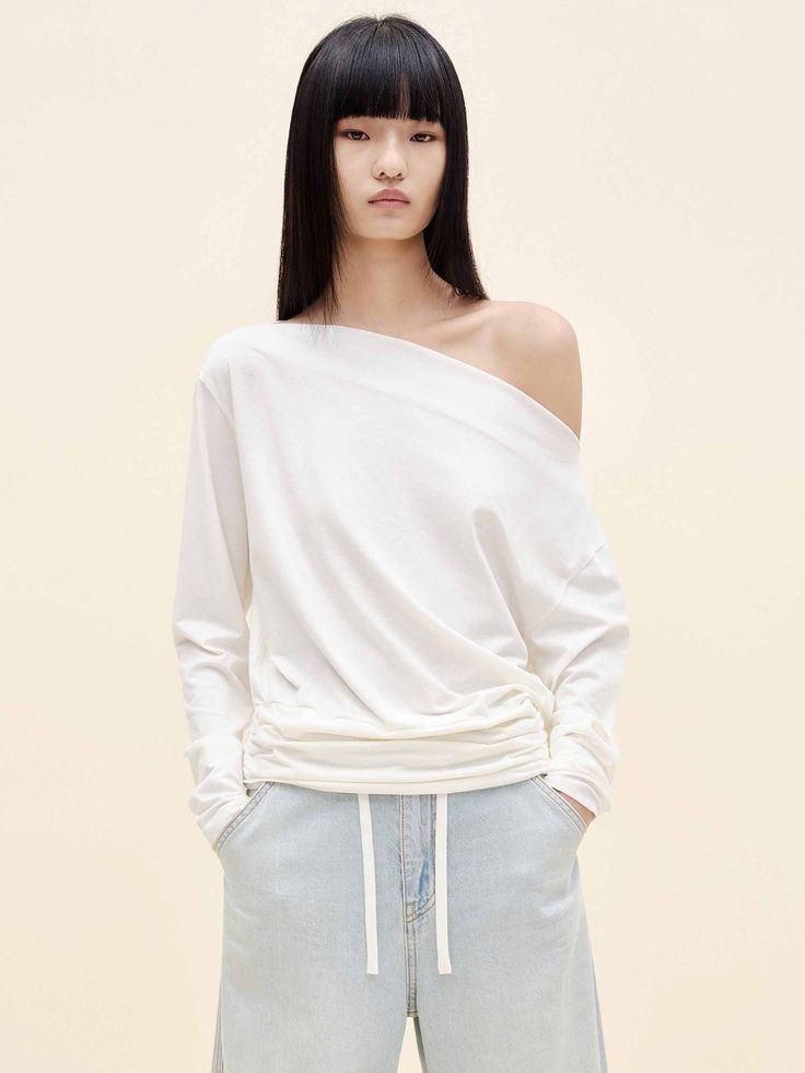 Woman with long black hair wearing an off-shoulder white top and light wash jeans