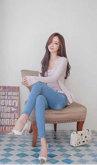 Woman with long hair wearing blue jeans and white heels, sitting on a chair indoors