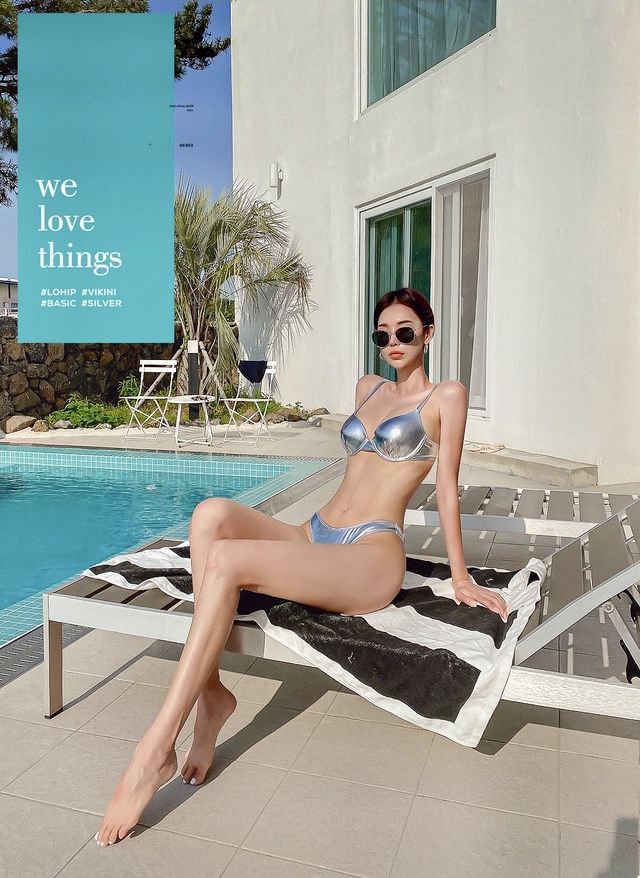 Woman in a silver bikini and sunglasses posing by a pool