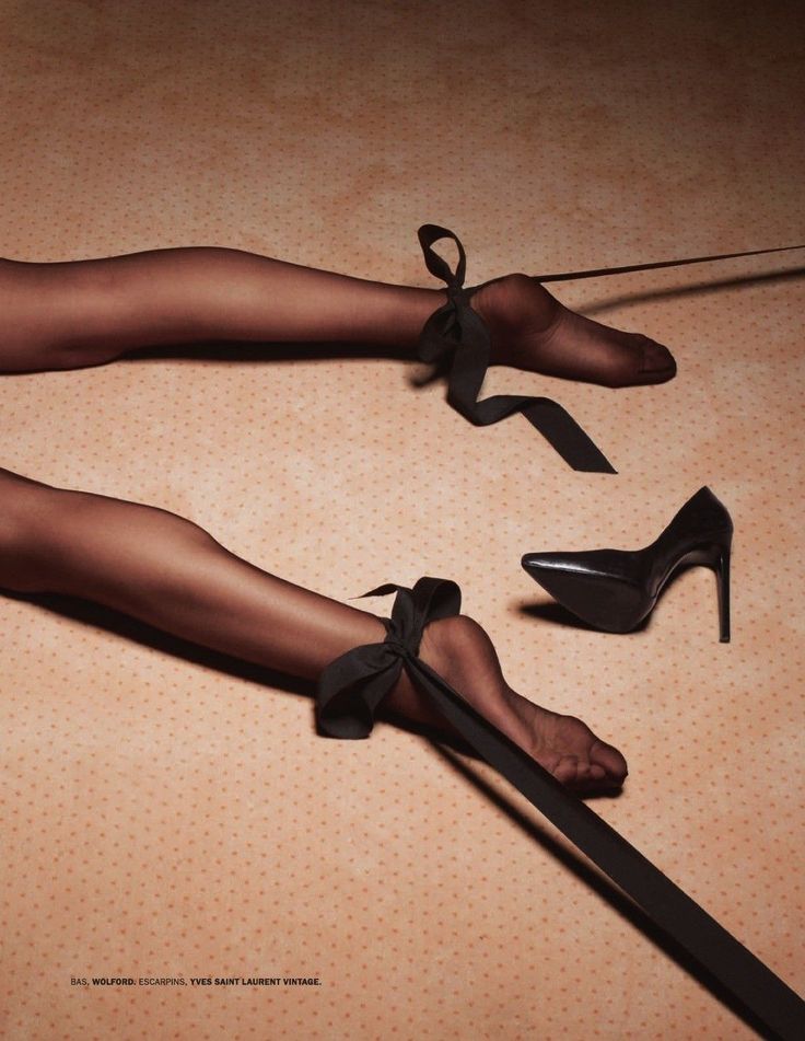 Legs in black stockings with ankles tied by black ribbons, next to a high heel