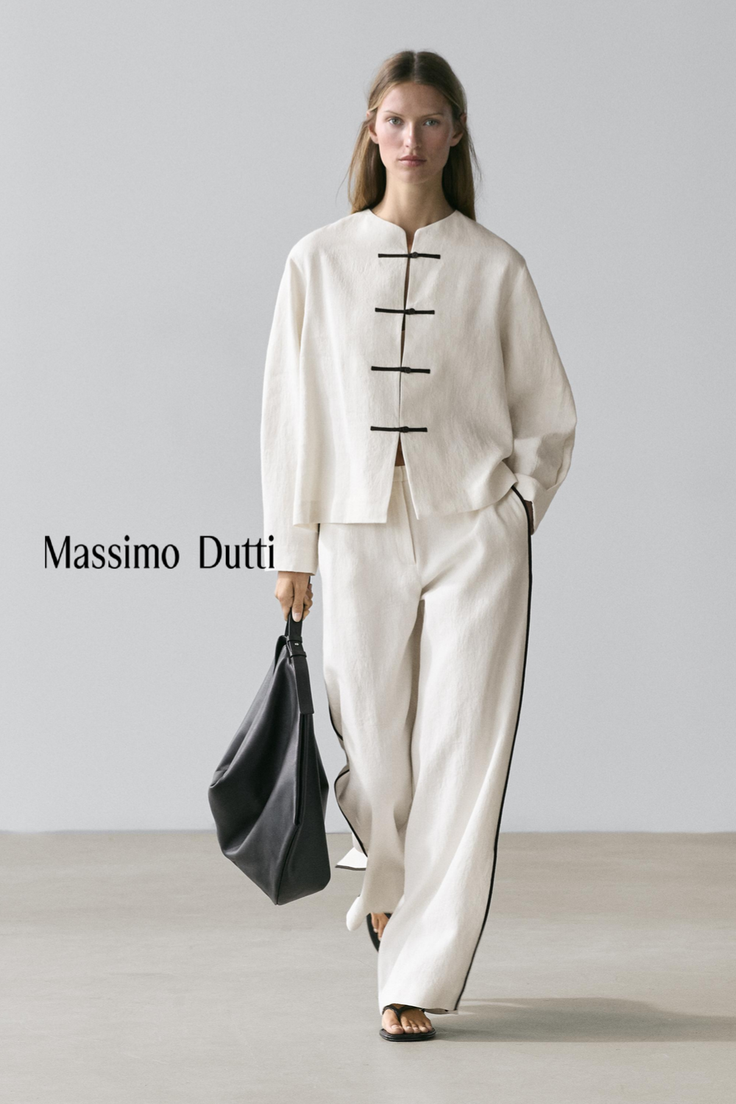 Woman in a white top and wide-leg pants holding a black handbag