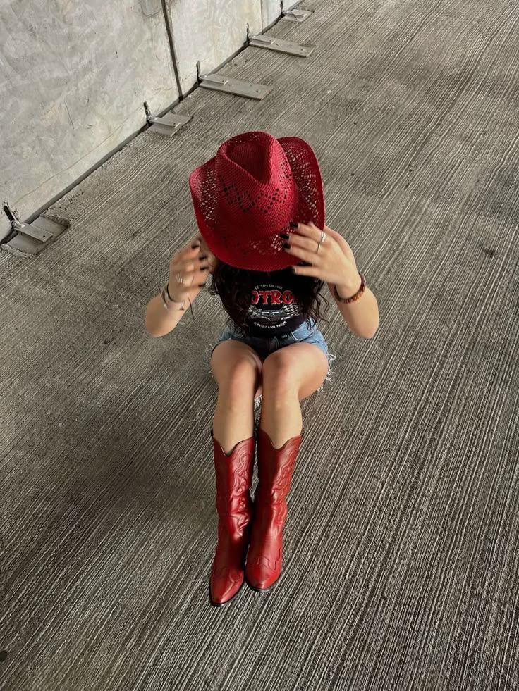 Person in a red cowboy hat and boots sitting on a textured concrete surface