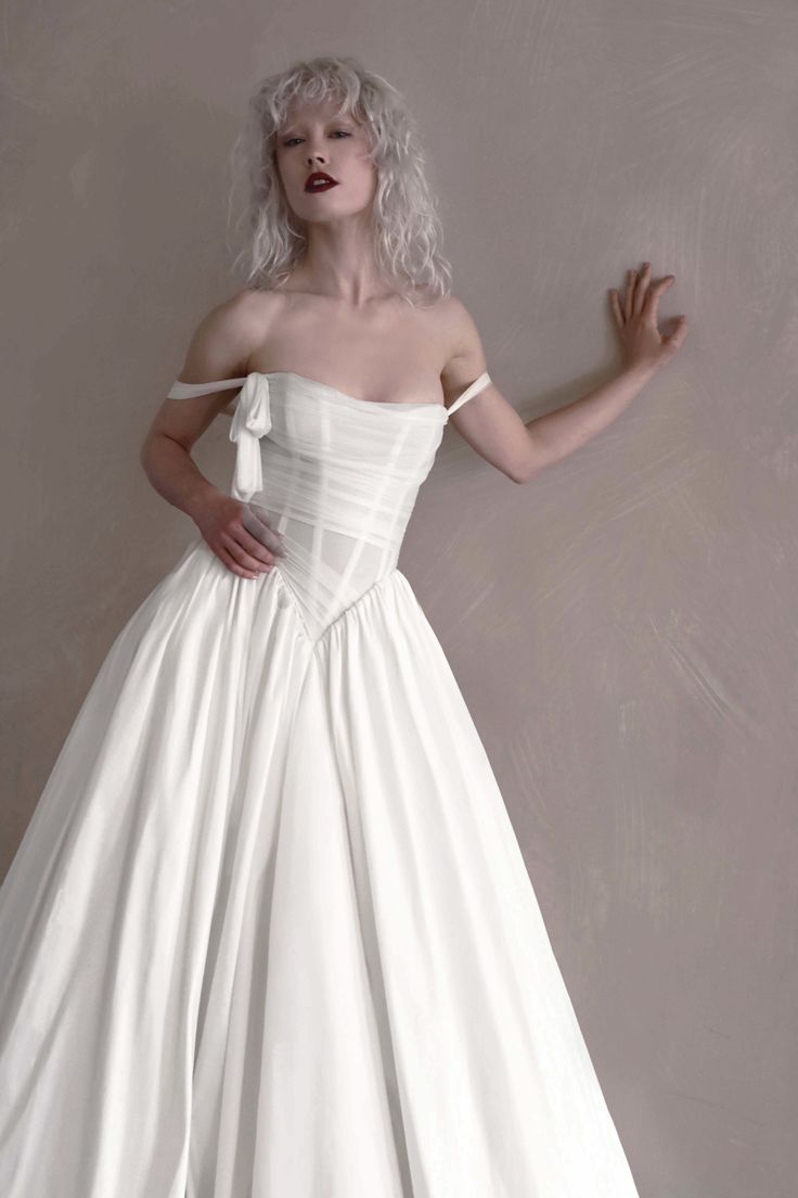Woman with blonde curly hair wearing a white strapless dress indoors