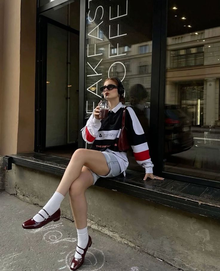 Woman in a long sleeve shirt and denim shorts sitting on a ledge outdoors