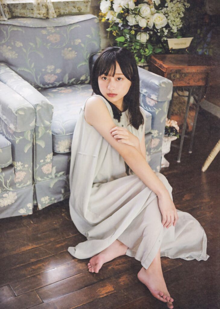Woman with long hair in a sleeveless dress sitting on a wooden floor indoors