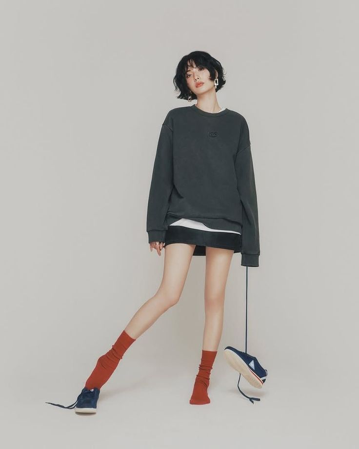 Woman with short hair wearing an oversized sweatshirt and mini skirt with red socks