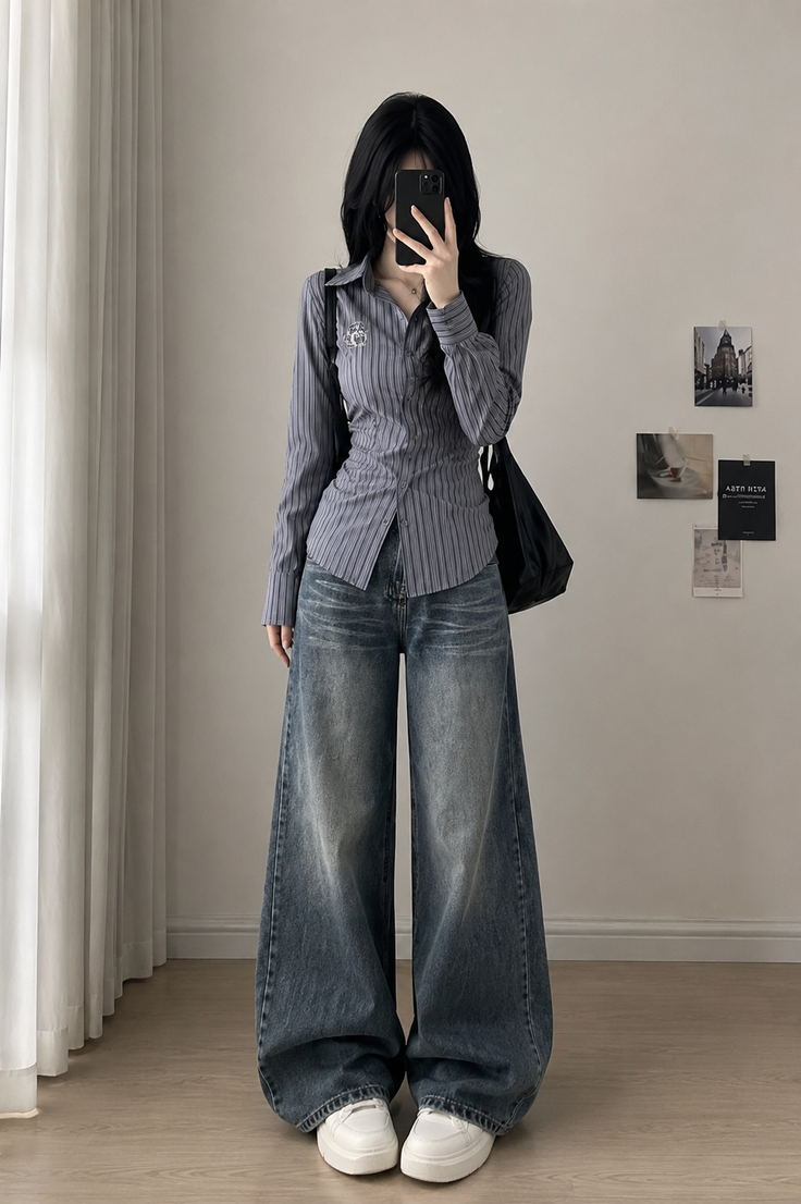 Person with long black hair wearing a striped shirt and wide leg jeans indoors