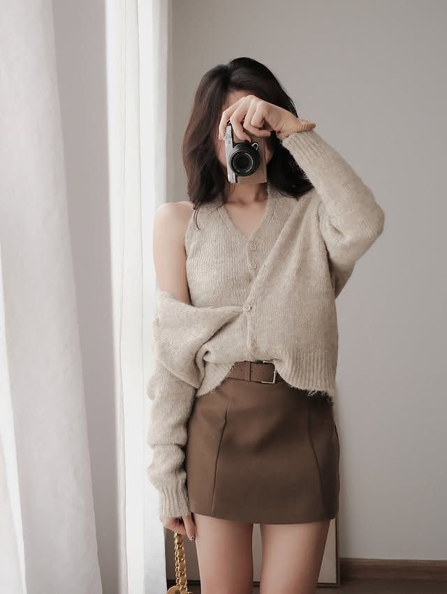 Woman in a cardigan and mini skirt holding a camera indoors