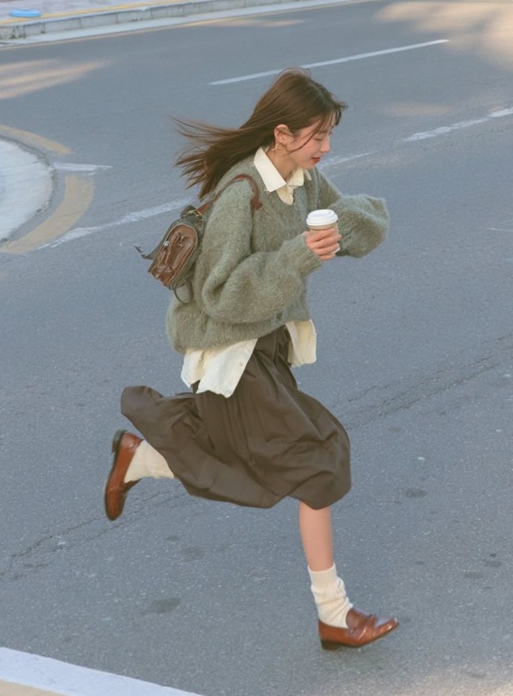 Woman in a sweater and skirt running on a street with a coffee cup