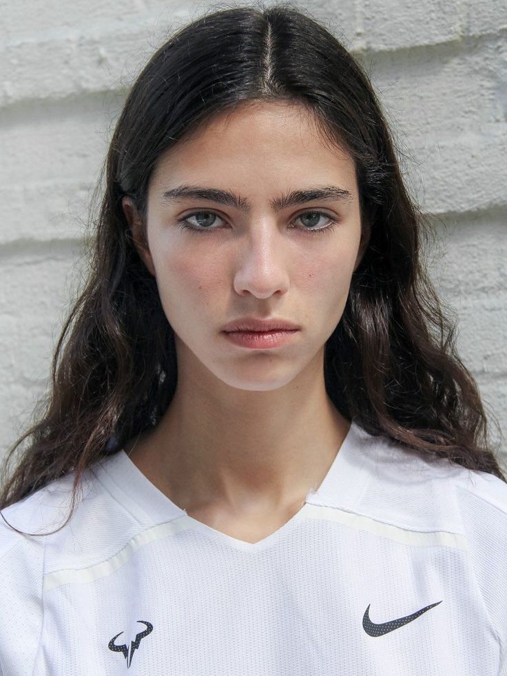Woman with long dark hair wearing a white shirt, looking directly at the camera