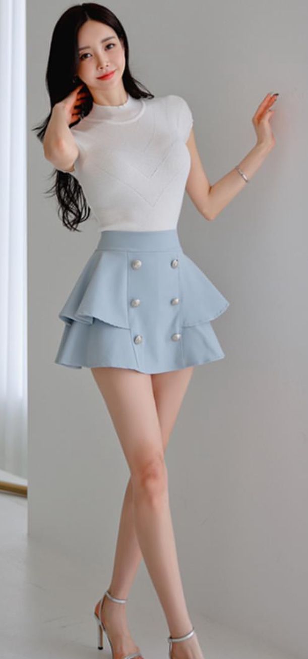 Woman with long black hair wearing a white top and blue mini skirt indoors