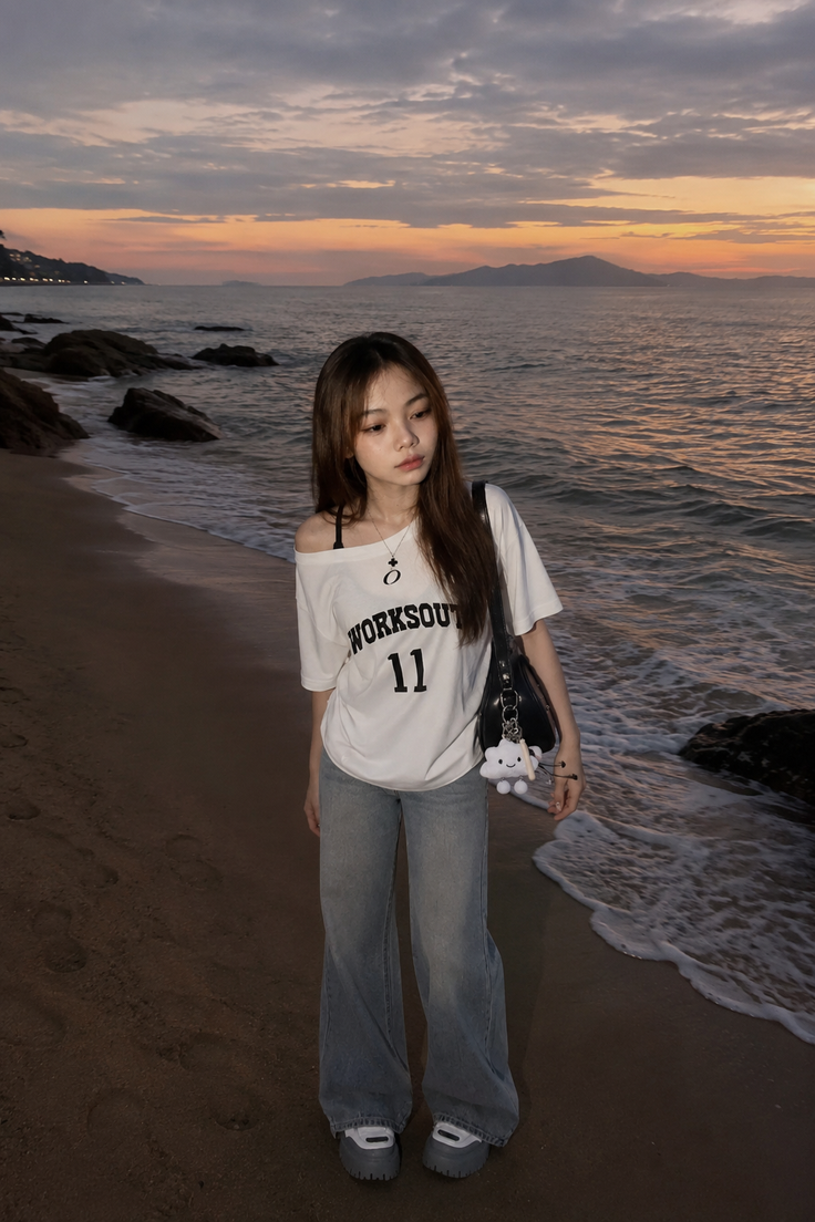 Woman in an off-shoulder top and jeans on a beach at sunset