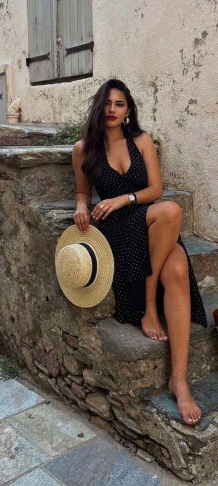 Woman in a polka dot dress sitting on stone steps, holding a straw hat