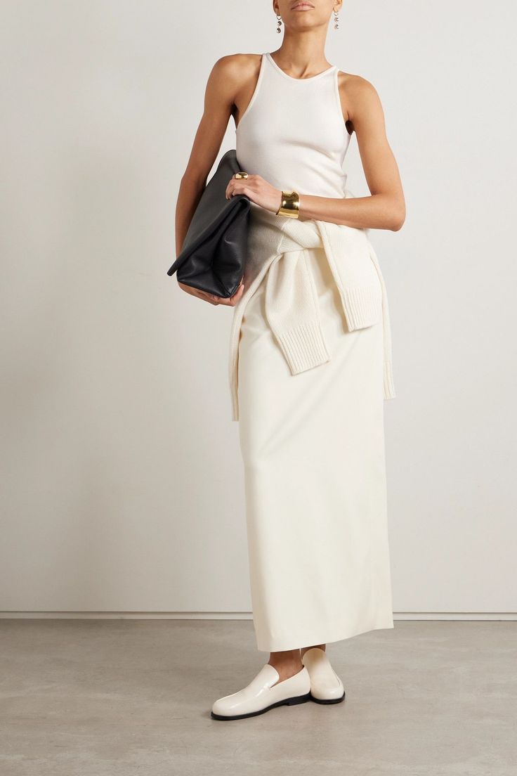 Woman in a white tank top and long skirt holding a black clutch bag