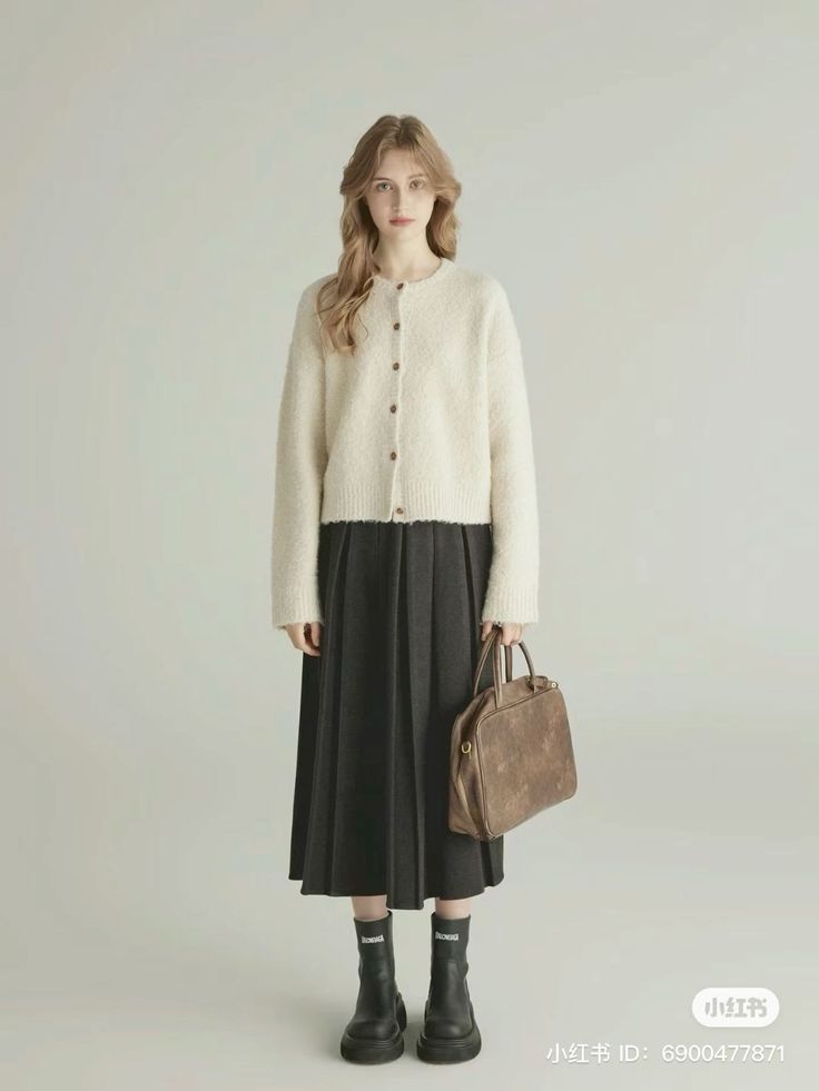 Woman in a cream cardigan and dark pleated skirt holding a brown bag