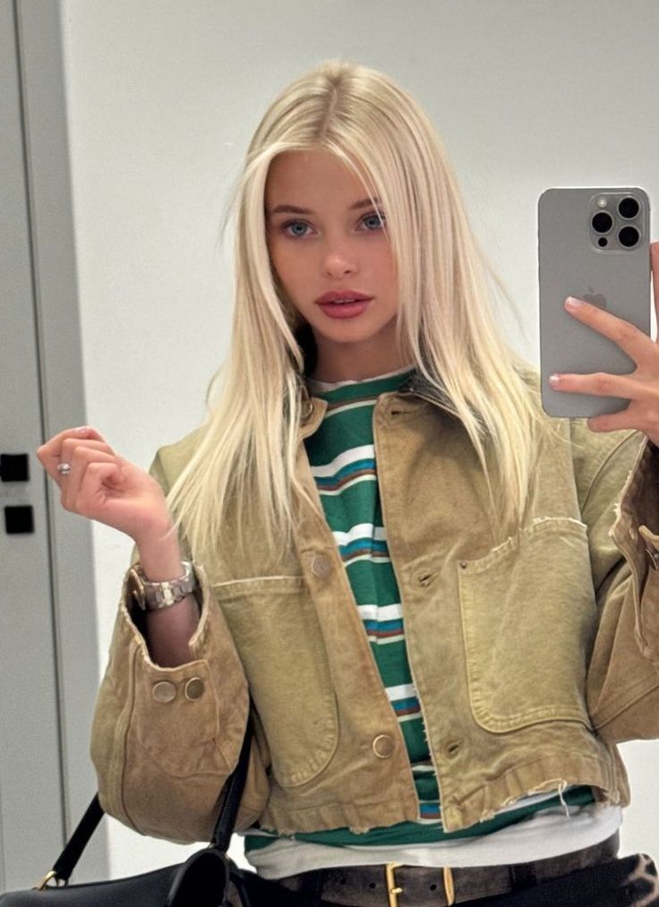 Blonde woman in a cropped jacket and striped shirt taking a mirror selfie