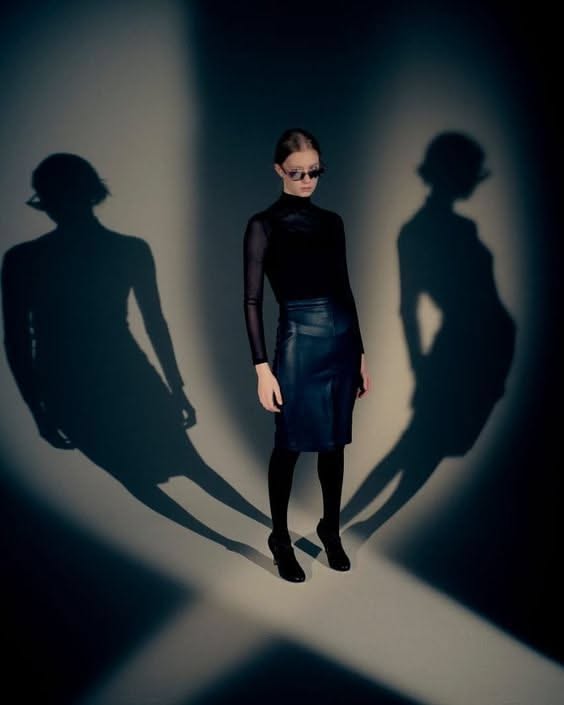 Woman in a black top and leather skirt with dramatic shadows