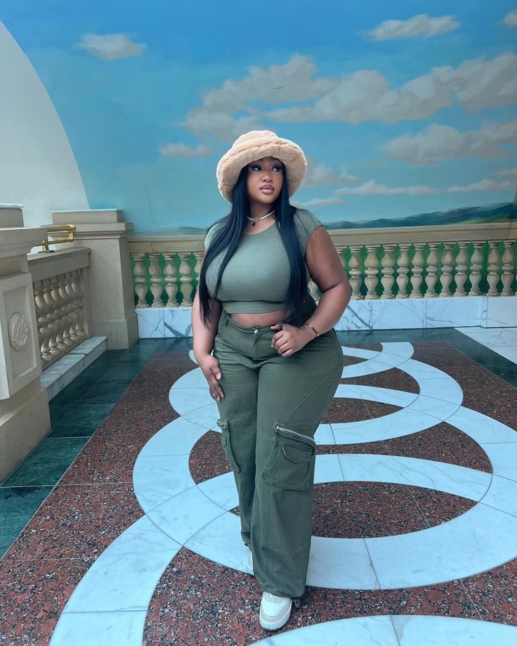 Woman in a green crop top and cargo pants with a fuzzy bucket hat indoors