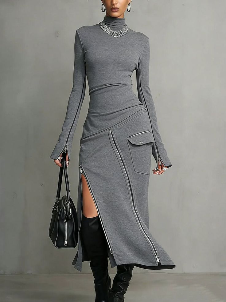 Woman in a gray dress with zipper details and black boots holding a handbag